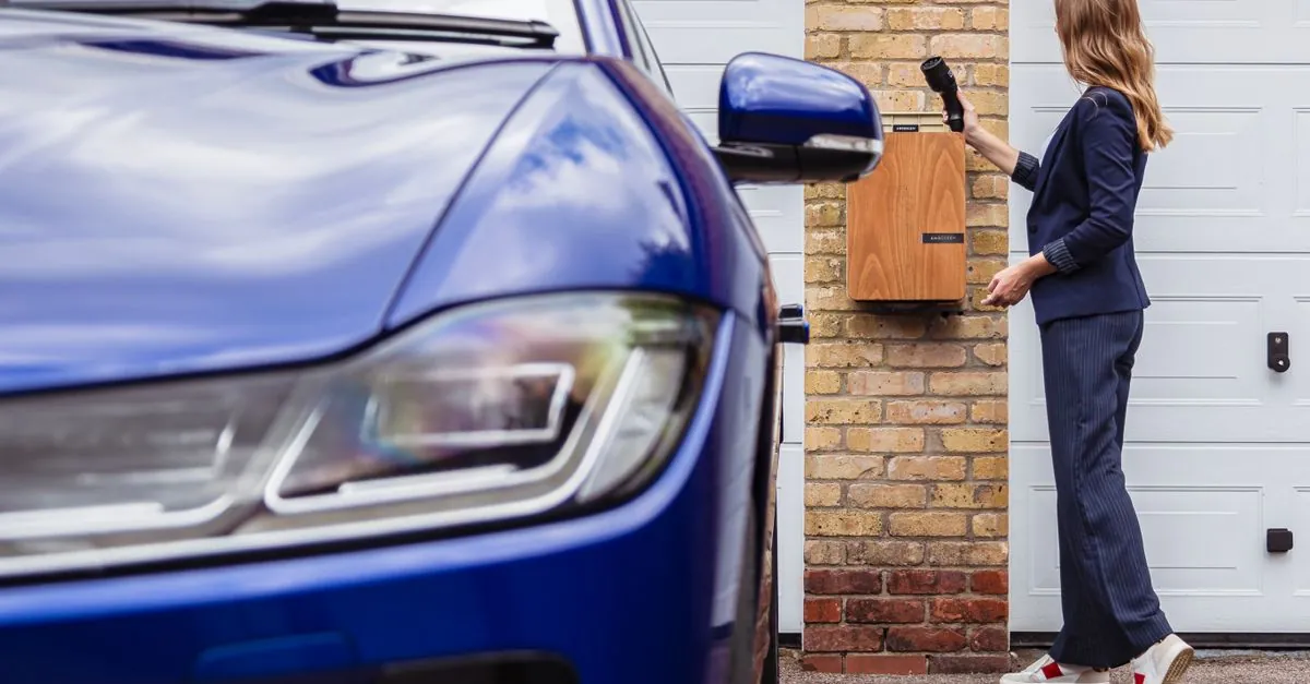 Laadpaal aan de gevel tussen twee garagepoorten, naast een elektrische wagen