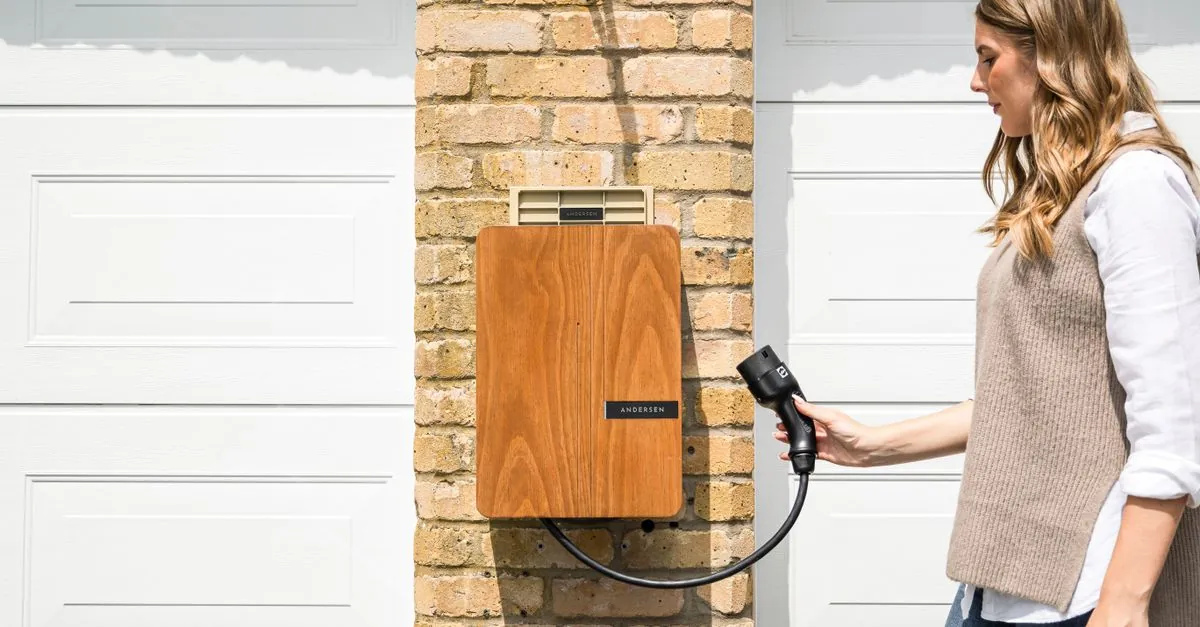 Vrouw neemt de laadkabel van een houten wallbox aan een bakstenen gevel